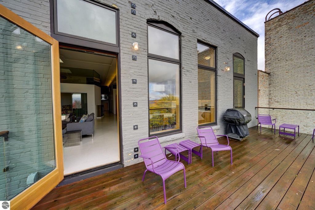Modern condo balcony with purple chairs, wooden deck, and large glass doors leading to a stylish interior, showcasing views of Traverse City.