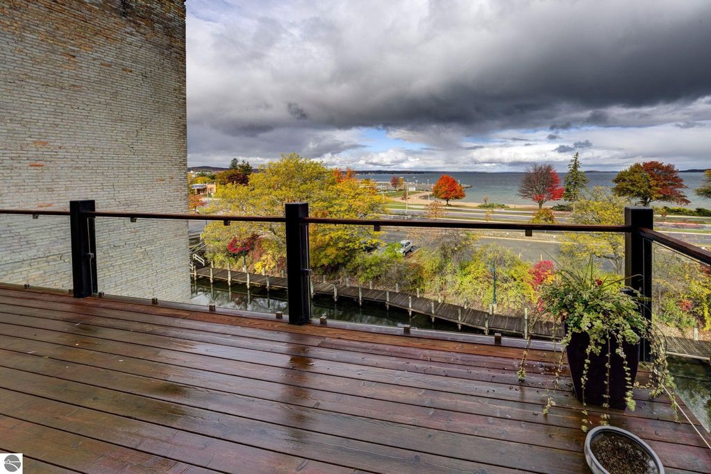 Modern balcony view overlooking Traverse City bay, featuring lush autumn foliage, wooden deck, and cloudy sky.
