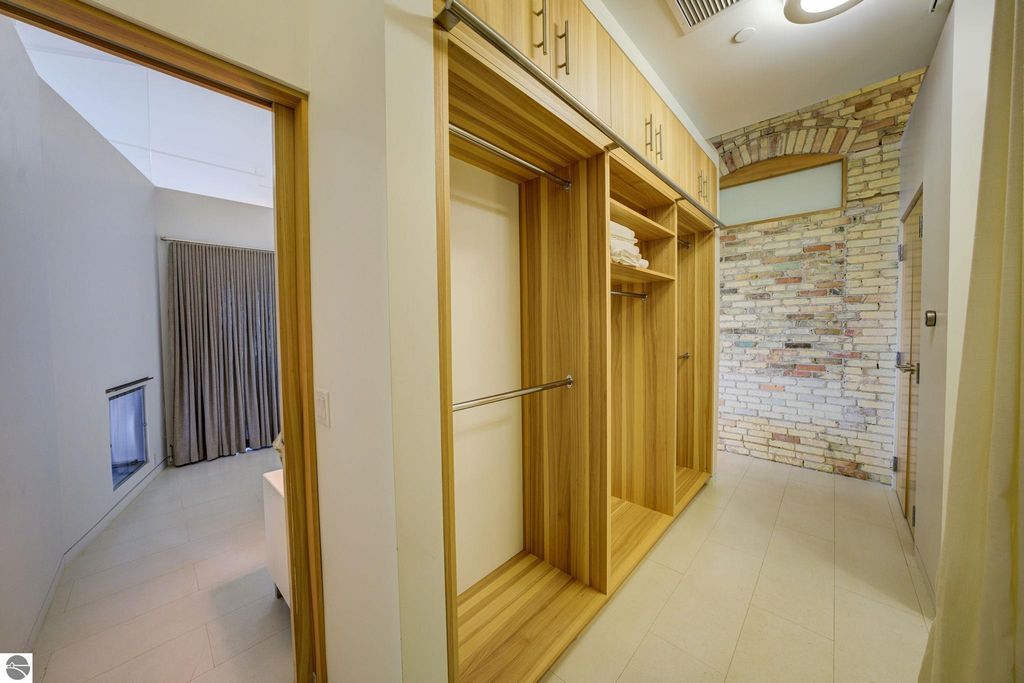 Modern interior hallway featuring wooden closets with shelves and hanging space, leading to a room with large curtains and a stone accent wall, highlighting the contemporary design of the downtown Traverse City condo.