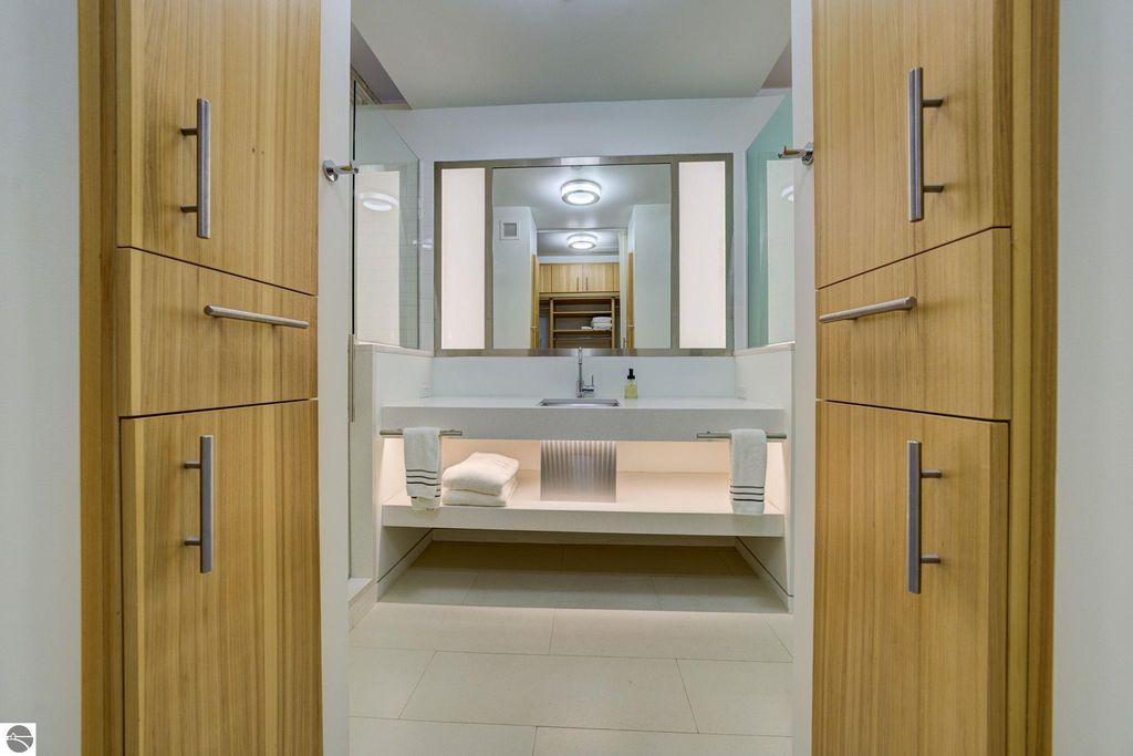 Modern bathroom interior with wooden cabinetry, sleek sink, and neatly arranged towels, showcasing contemporary design elements in a Traverse City condo listing.
