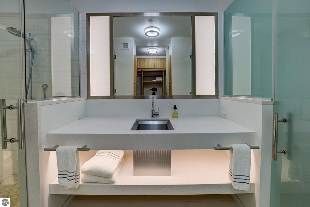 Modern bathroom vanity with sleek design, under-mount sink, illuminated mirrors, and glass shower enclosure, showcasing luxury features of the downtown Traverse City condo listing.