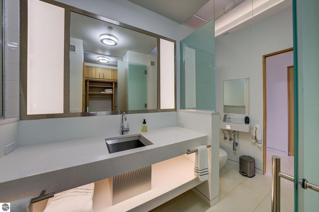 Modern bathroom interior featuring a sleek countertop sink, illuminated mirrors, and minimalist design elements, emphasizing luxury and contemporary aesthetics in the downtown Traverse City condo.