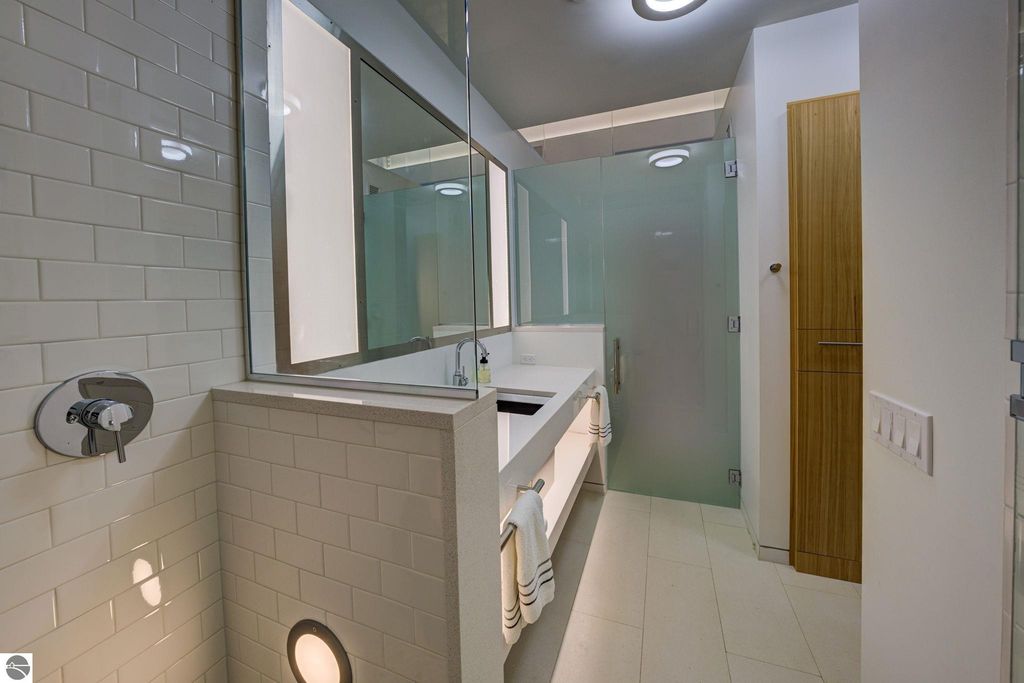 Modern bathroom design featuring sleek white subway tiles, a large mirror, glass shower enclosure, and contemporary fixtures, highlighting luxury and functionality in a downtown Traverse City condo.