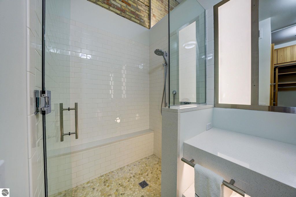 Modern bathroom featuring a glass shower enclosure, white subway tiles, stone flooring, and a sleek vanity with a towel rack, highlighting contemporary design elements in a downtown Traverse City condo.
