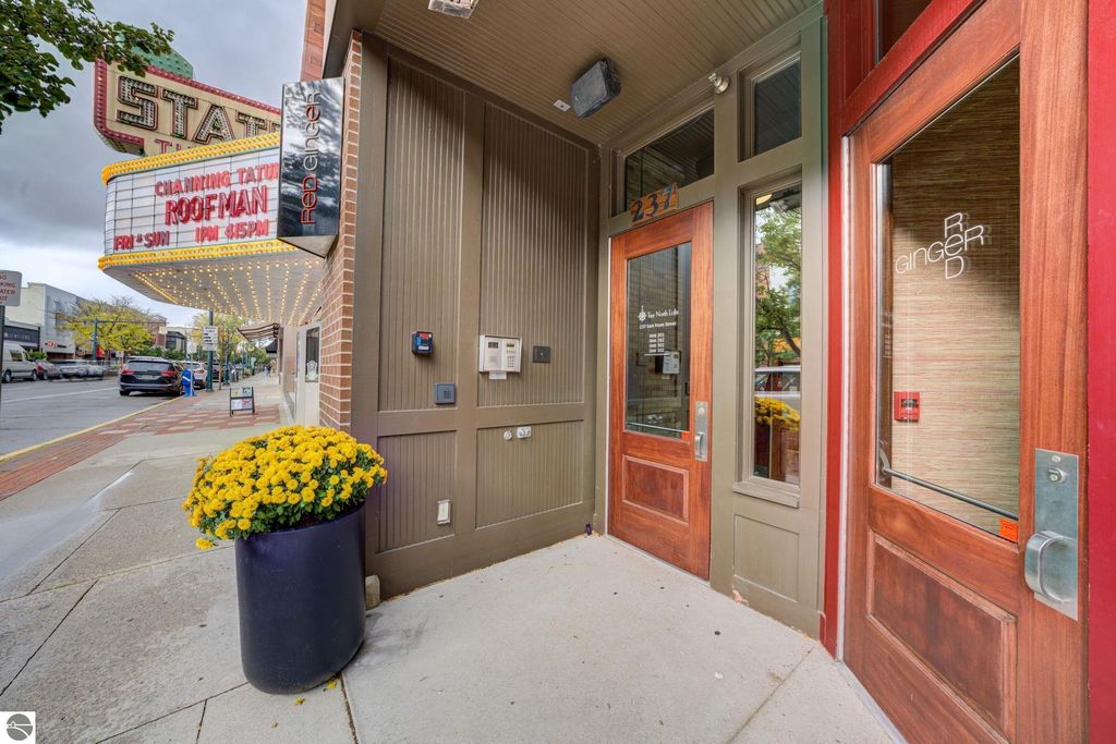 Entrance of a modern downtown condo at 237 E Front Street, Traverse City, featuring a vibrant flower pot, nearby theater marquee, and inviting wooden doors, highlighting the property's prime location near restaurants and the beach.