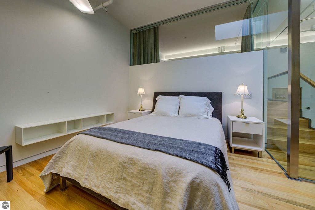 Modern bedroom in downtown Traverse City condo, featuring a queen bed, minimalist decor, hardwood floors, and contemporary lighting, highlighting spacious design and comfort.