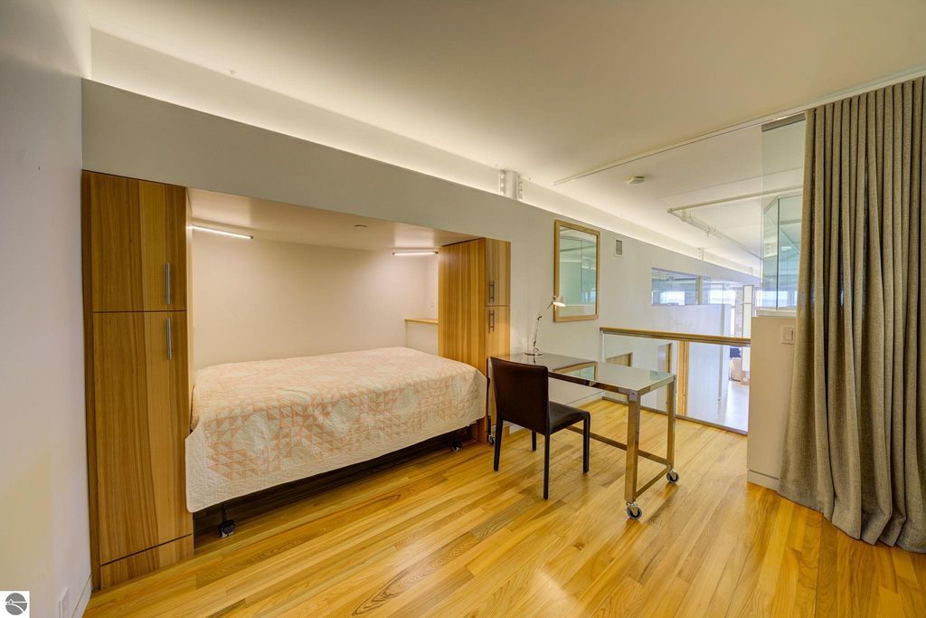 Modern downtown condo interior featuring a compact bedroom with a wall bed, wooden cabinetry, a small desk, and hardwood flooring, emphasizing contemporary design and functionality.