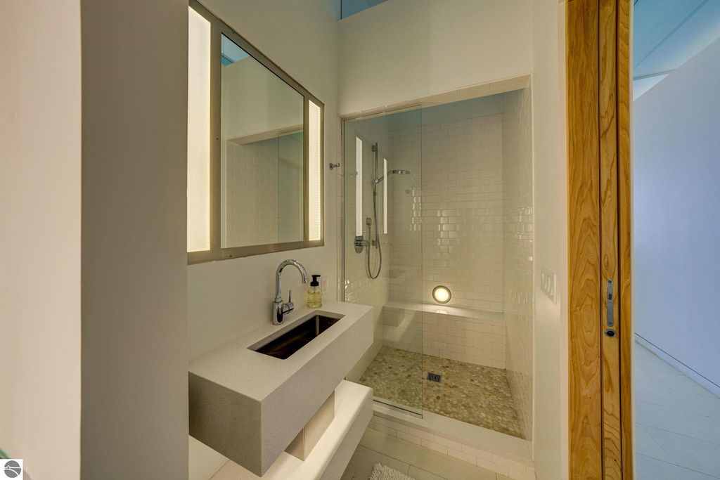 Modern bathroom featuring a sleek vanity with integrated sink, large mirror, and spacious walk-in shower with glass enclosure, emphasizing contemporary design elements and natural light.