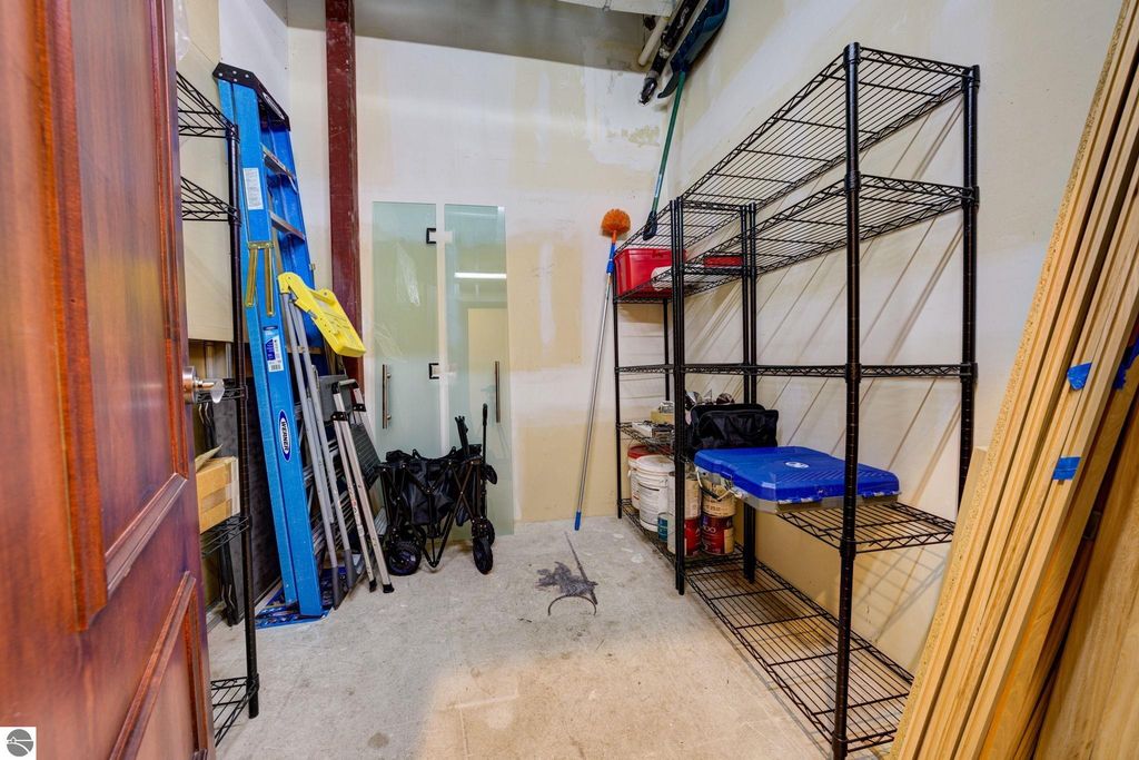 Storage area with shelving units, cleaning supplies, and a ladder, featuring a door leading to another room, relevant to the modern downtown condo listing at 237 E Front Street, Traverse City.