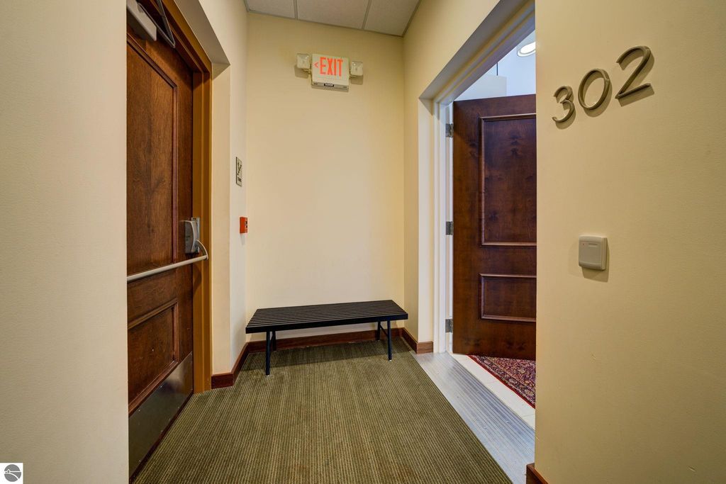Condo entrance hallway at 237 E Front Street, Traverse City, featuring door number 302, a wooden door, and a black bench on a carpeted floor, showcasing modern architecture and design elements.