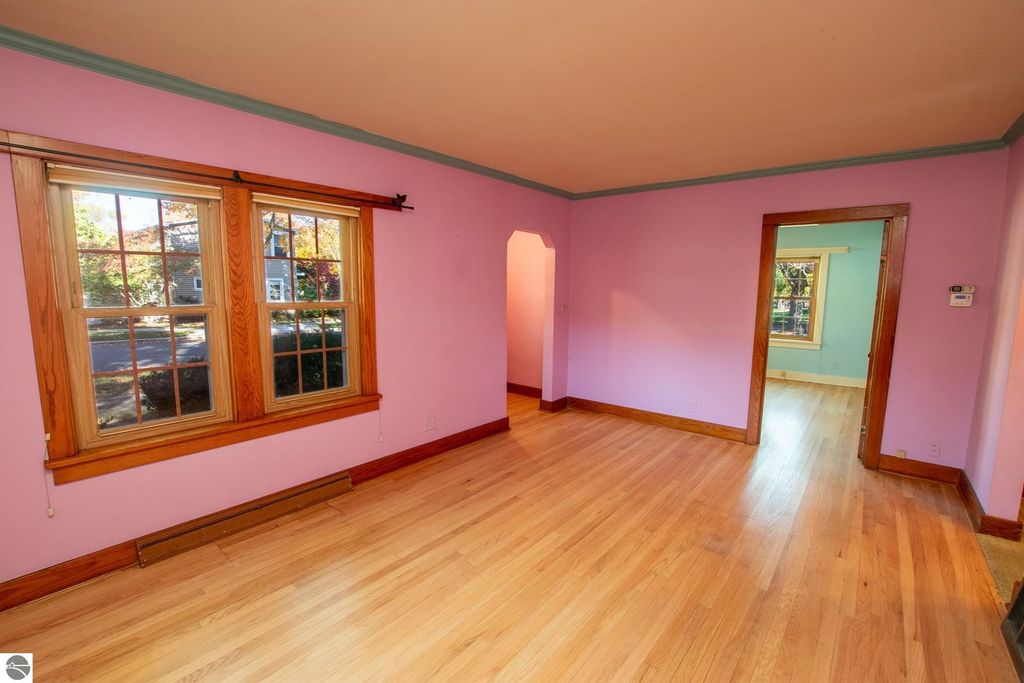 Interior view of a 2-bedroom ranch home for sale at 1101 Jefferson Avenue, featuring pink walls, wooden trim, and large windows allowing natural light, showcasing potential for renovation in Traverse City's Slabtown neighborhood.