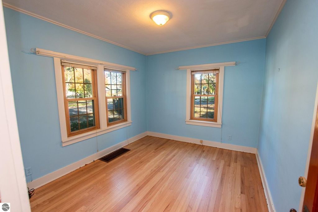 Interior view of a light blue room with hardwood flooring, featuring two windows allowing natural light, showcasing potential for renovation or design in a Traverse City property listing.