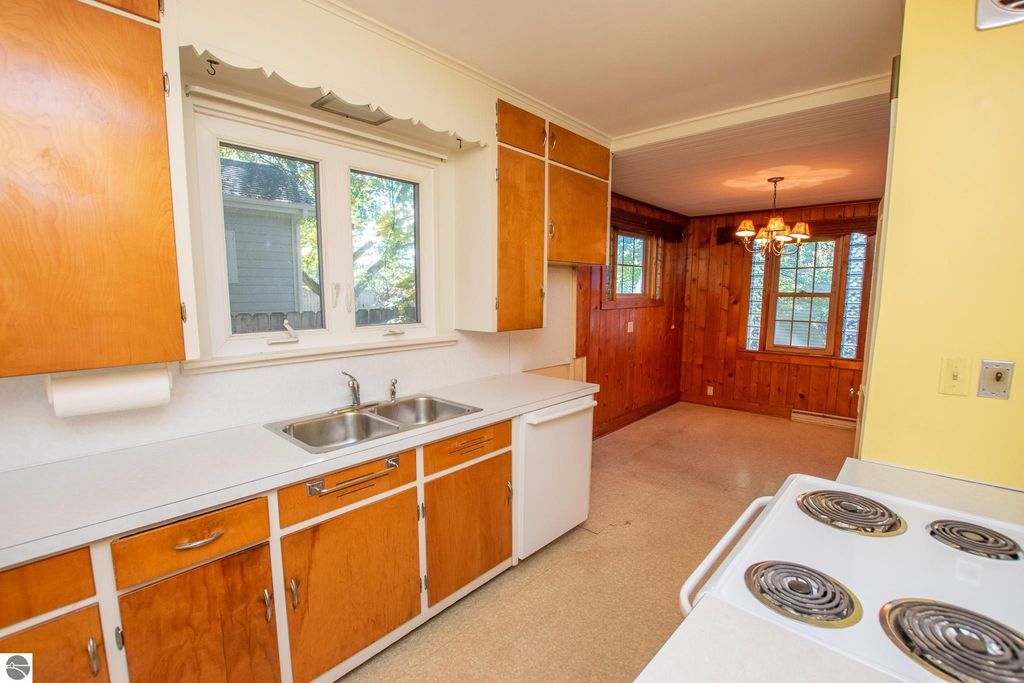 Kitchen interior featuring wooden cabinets, dual sink, and adjacent dining area with chandelier, showcasing potential for renovation in Traverse City home listing.