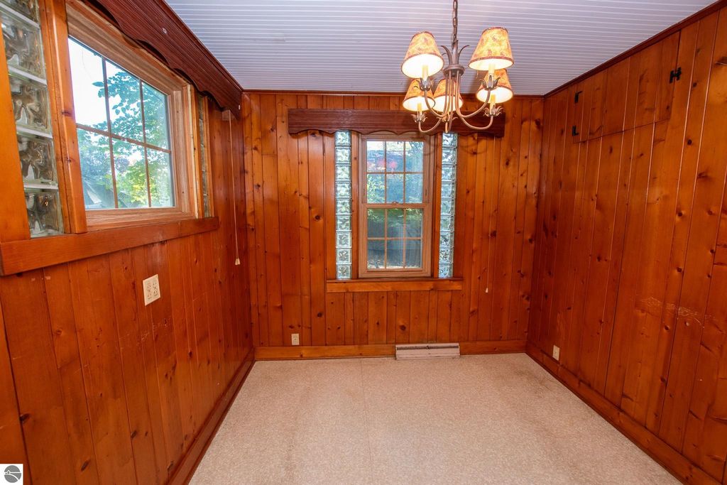 Interior view of a cozy room featuring wooden walls, a window with glass blocks, and a chandelier, suitable for renovation in a Traverse City property listing.