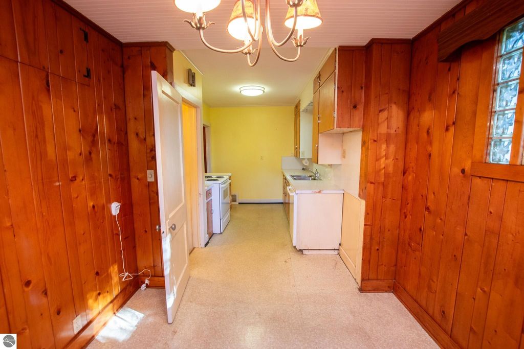 Interior view of a kitchen space featuring wooden paneling, a chandelier, and appliances including a stove and refrigerator, showcasing the potential for renovation in a Traverse City property listing.