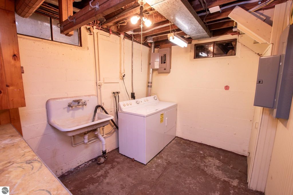 Basement laundry area featuring a washing machine, utility sink, and electrical panel, part of the 2-bedroom ranch home at 1101 Jefferson Avenue, Traverse City, MI.