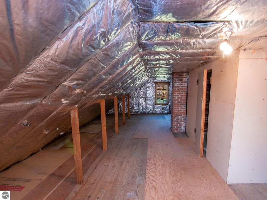 Attic interior with exposed wooden beams, insulated walls, and a window, showcasing renovation potential for the property at 1101 Jefferson Avenue, Traverse City, MI.