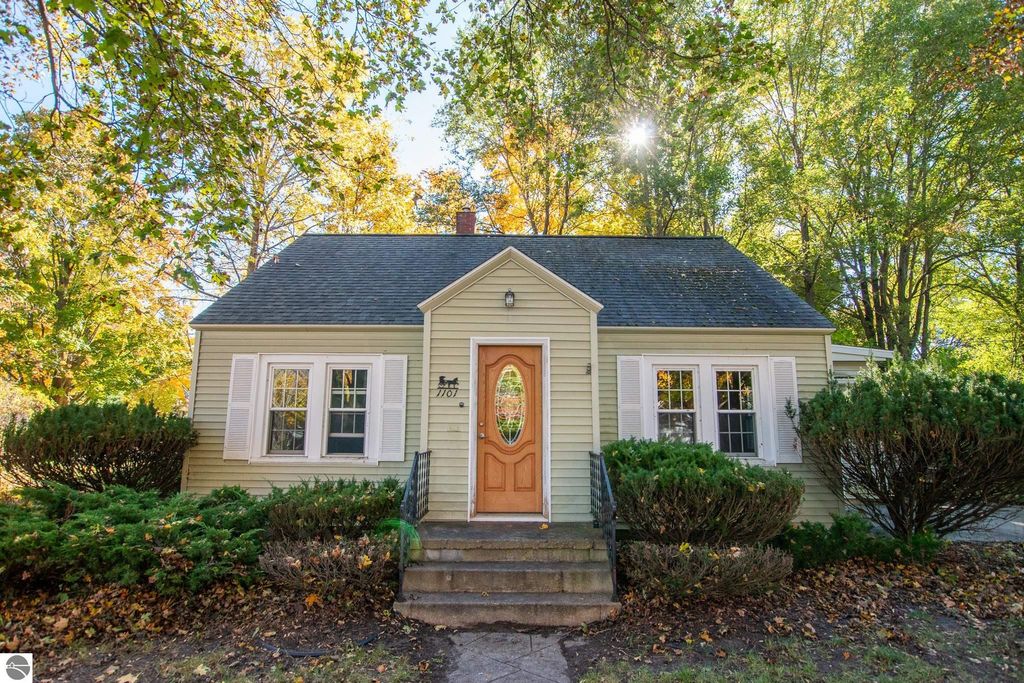 Charming 2-bedroom ranch home at 1101 Jefferson Avenue, Traverse City, surrounded by lush greenery and autumn foliage, showcasing a welcoming front entrance and large lot, ideal for renovation or new construction.