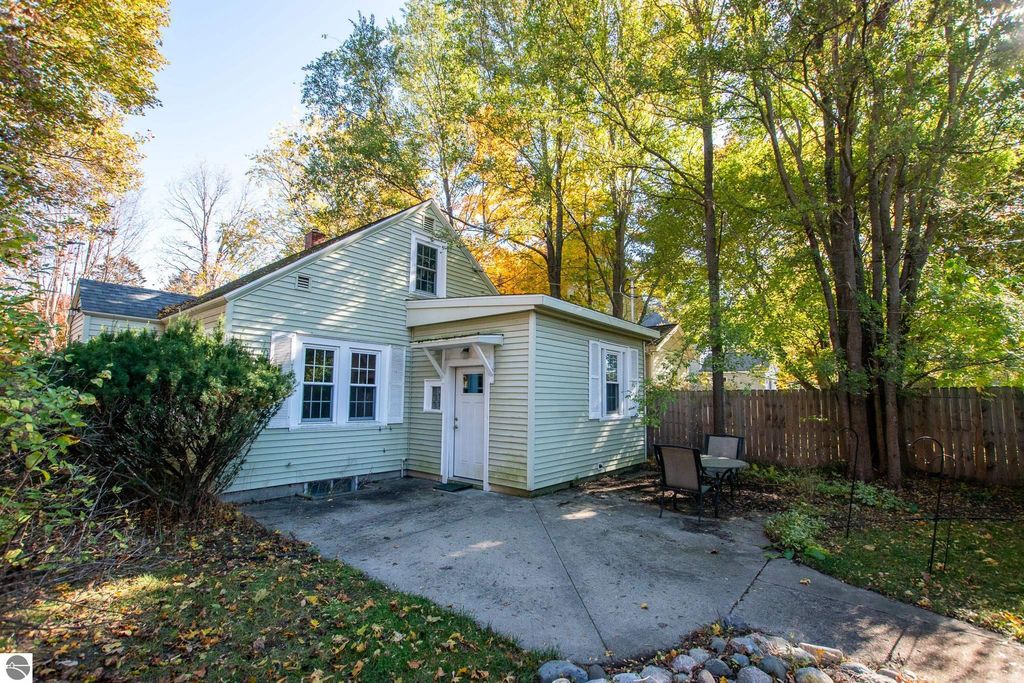 Two-bedroom ranch home at 1101 Jefferson Avenue, Traverse City, surrounded by trees and outdoor seating area, showcasing potential for renovation or new construction on oversized lot.