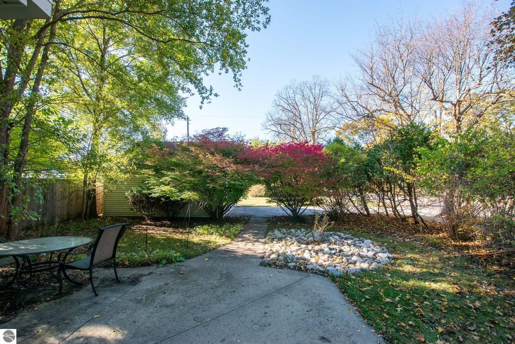 Outdoor view of landscaped yard at 1101 Jefferson Avenue, featuring a stone pathway, seating area, and colorful foliage, highlighting the potential for home renovation or development in Traverse City's Slabtown neighborhood.