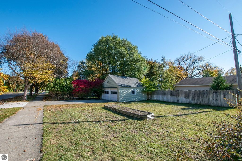 Oversized lot at 1101 Jefferson Avenue in Traverse City, featuring a single-story ranch home, surrounded by trees and colorful foliage, with a clear blue sky above.