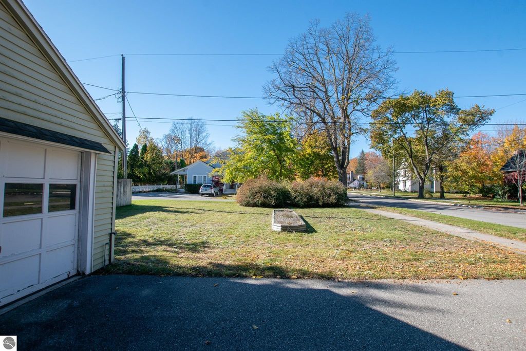 View of a spacious lot at 1101 Jefferson Avenue in Traverse City, showcasing a garage, grassy area, and surrounding trees, emphasizing the potential for renovation or new construction in a desirable neighborhood.