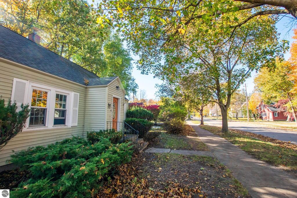 Exterior view of a 2-bedroom ranch home at 1101 Jefferson Avenue, Traverse City, MI, showcasing a landscaped front yard with shrubs and trees, highlighting the neighborhood's autumn foliage and nearby sidewalk.