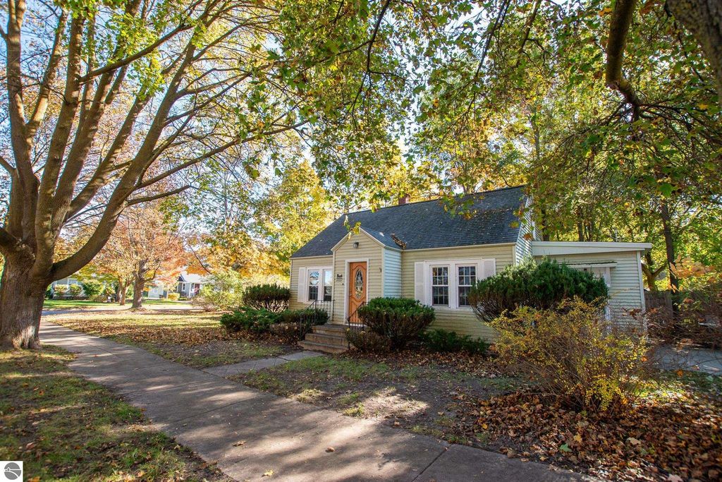 Two-bedroom ranch home at 1101 Jefferson Avenue, Traverse City, surrounded by trees and autumn foliage, showcasing potential for renovation or new construction on oversized lot.