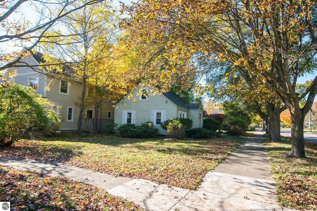 Charming 2-bedroom ranch home at 1101 Jefferson Avenue, surrounded by vibrant fall foliage, showcasing a spacious lawn and sidewalk in Traverse City's Slabtown neighborhood.