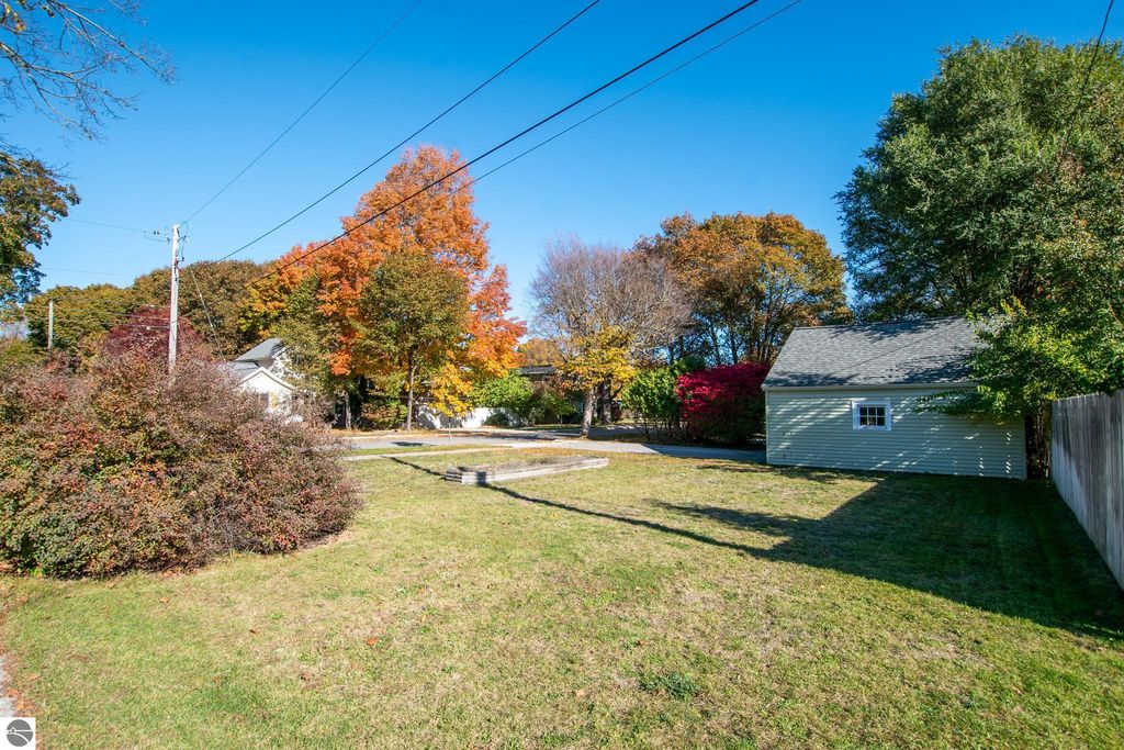 Oversized lot at 1101 Jefferson Avenue, Traverse City, showcasing vibrant autumn foliage, grassy area, and surrounding residential structures, ideal for renovation or new construction opportunities.