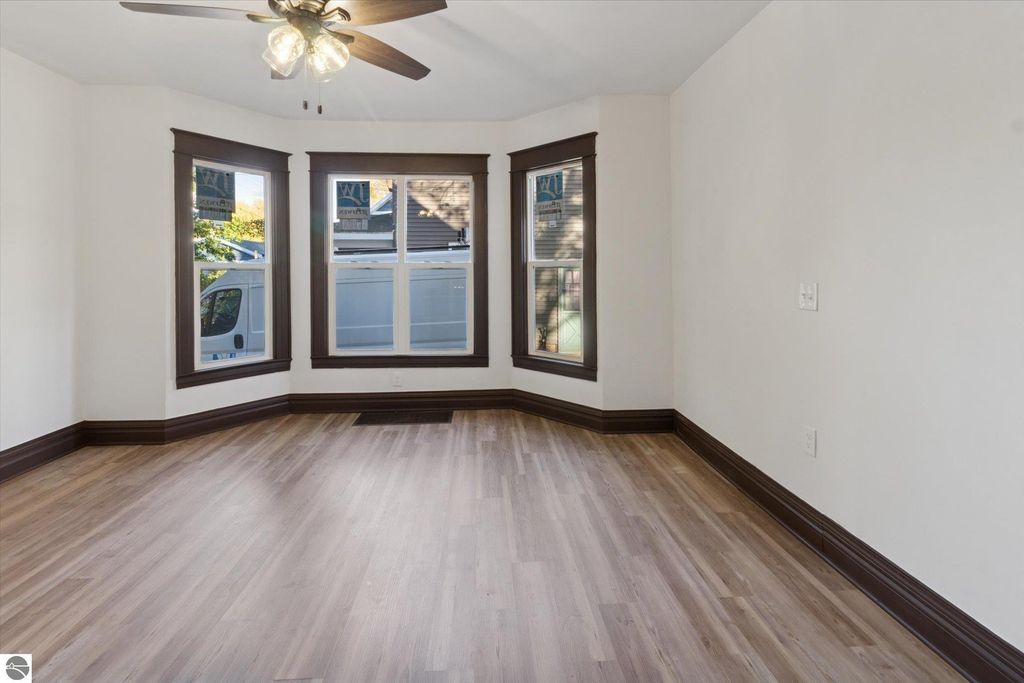 Renovated living room with large bay windows, new luxury vinyl plank flooring, and ceiling fan in a home at 117 E Wright Avenue, Shepherd, MI.