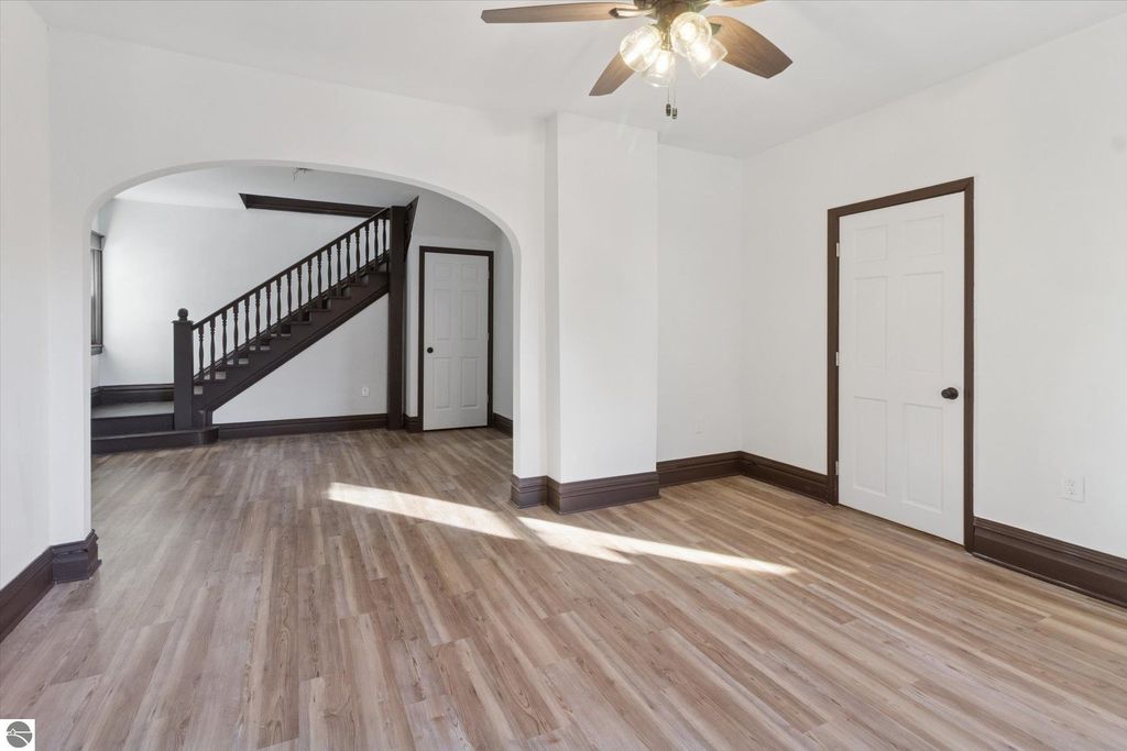 Renovated living space in Shepherd, MI, featuring new luxury vinyl plank flooring, ceiling fan, and arched doorway leading to staircase, showcasing the home's modern updates.