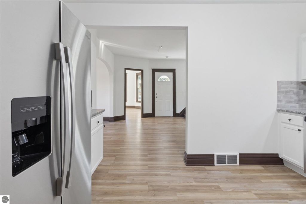 Renovated kitchen with stainless steel refrigerator, granite countertops, and view into the open living space of a 3-bedroom home in downtown Shepherd, MI.