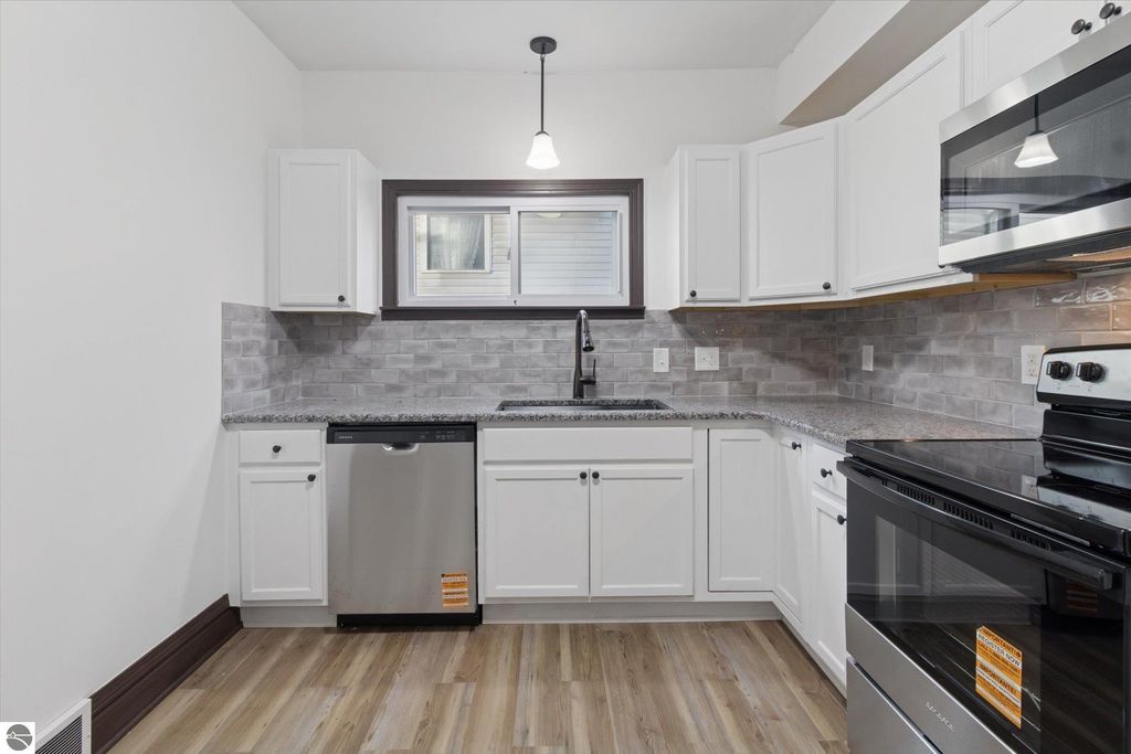 Renovated kitchen featuring white cabinetry, granite countertops, stainless steel appliances, and modern fixtures in a home at 117 E Wright Avenue, Shepherd, MI.
