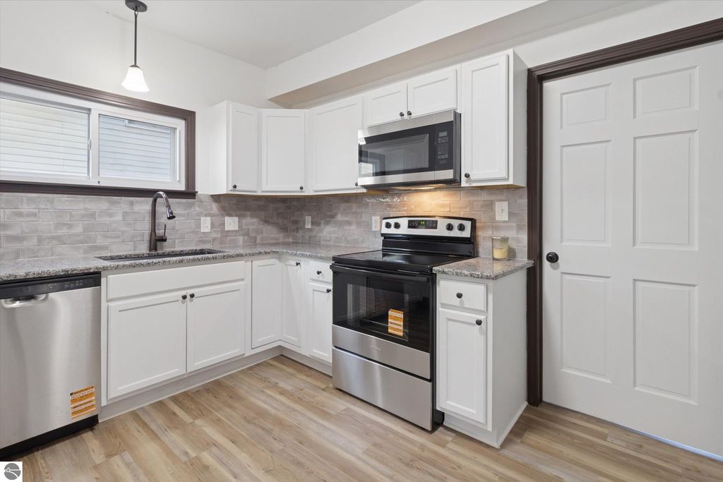 Renovated kitchen featuring stainless steel appliances, granite countertops, white cabinetry, and modern fixtures in a 3-bedroom home at 117 E Wright Avenue, Shepherd, MI.
