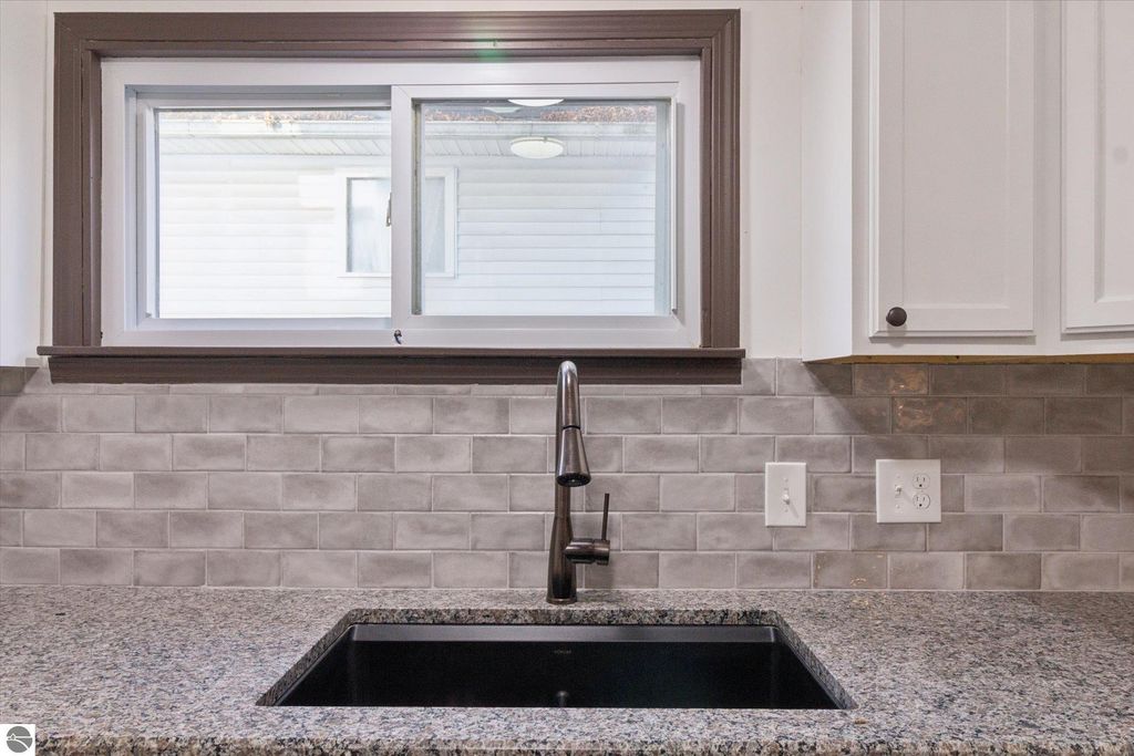Gorgeous kitchen sink area featuring a modern black sink, sleek faucet, and stylish gray tiled backsplash, showcasing the recent renovations of the 3-bedroom home at 117 E Wright Avenue, Shepherd, MI.