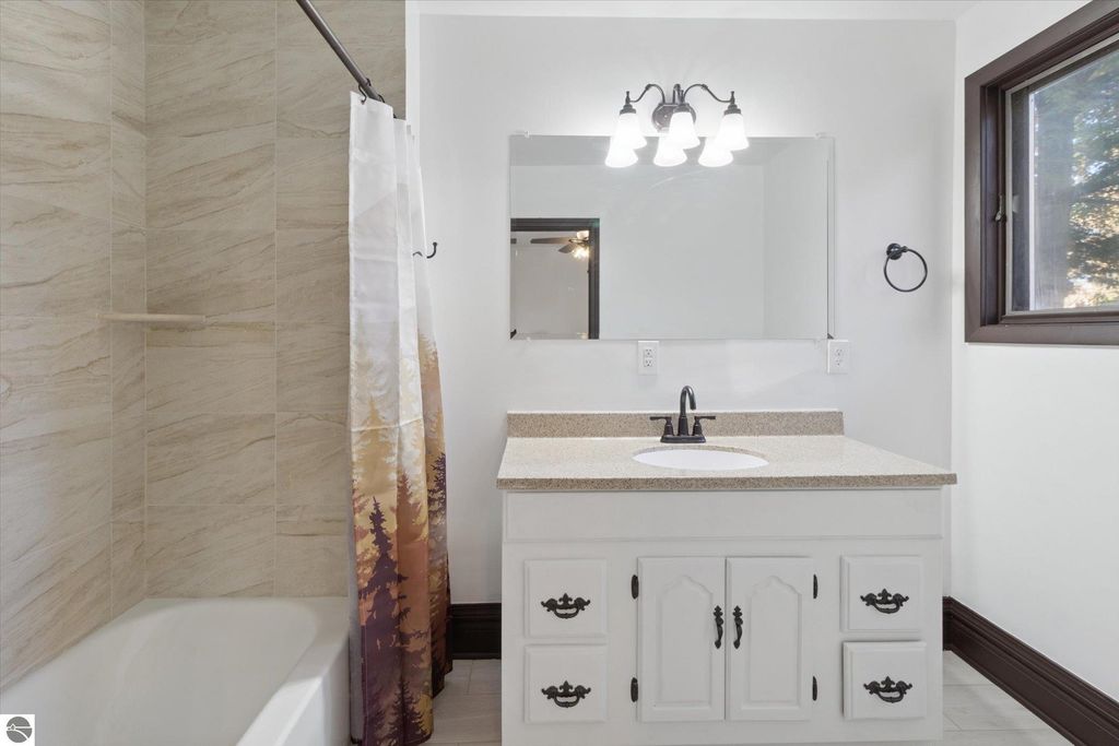Renovated bathroom featuring a modern vanity with granite countertop, mirror, and stylish lighting, complemented by a tiled shower and a bathtub, showcasing the home's updates at 117 E Wright Avenue, Shepherd, MI.