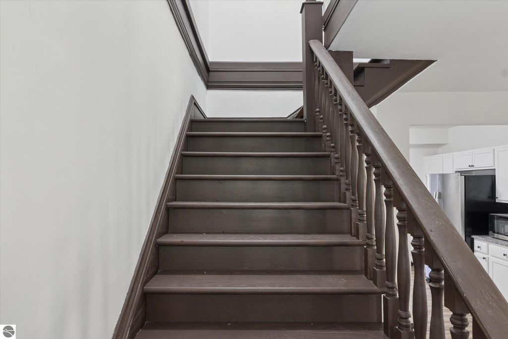 Staircase leading to the upper level of a renovated home at 117 E Wright Avenue, featuring dark wooden steps and a decorative banister, showcasing the interior design of the property listed for sale in Shepherd, MI.