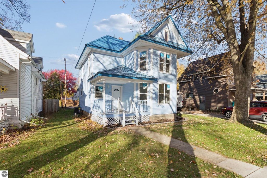 Renovated blue two-story home at 117 E Wright Avenue, Shepherd, MI, featuring a new metal roof, updated siding, and surrounded by autumn foliage.