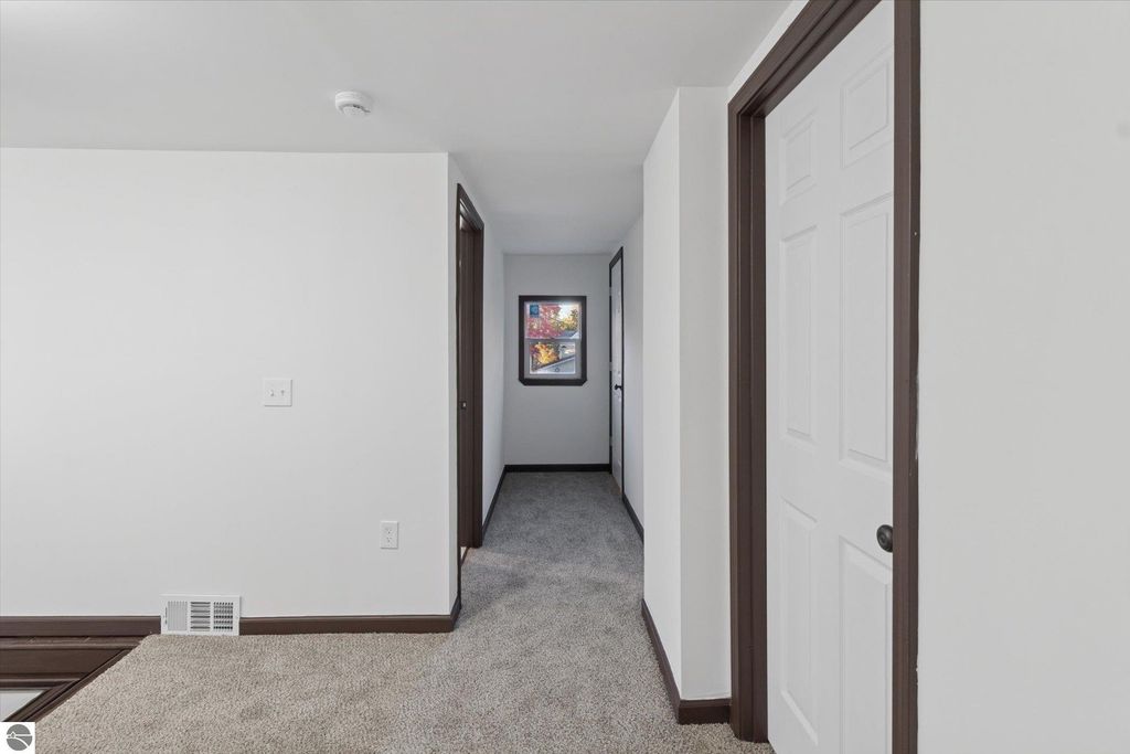 Renovated interior hallway of a 3-bedroom home in Shepherd, MI, featuring new carpeting, white walls, and dark trim, with a window at the end showcasing natural light.