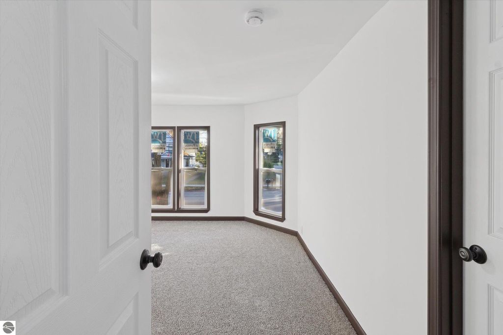 Renovated interior view of a room in a home at 117 E Wright Avenue, Shepherd, MI, featuring new carpet, white walls, and large windows with natural light.