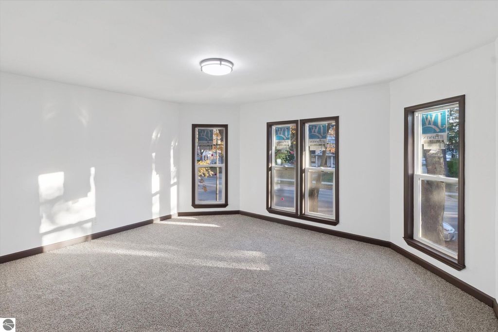 Bright and spacious living room in renovated home at 117 E Wright Avenue, featuring new carpet, large windows with street views, and modern lighting.
