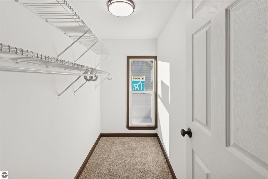 Walk-in closet with white shelving, window allowing natural light, and plush carpet in a renovated home at 117 E Wright Avenue, Shepherd, MI.