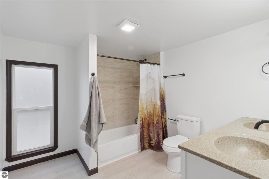 Renovated bathroom featuring a tub with shower, modern fixtures, granite countertop vanity, and a window, showcasing updates in the 3-bedroom home at 117 E Wright Avenue, Shepherd, MI.