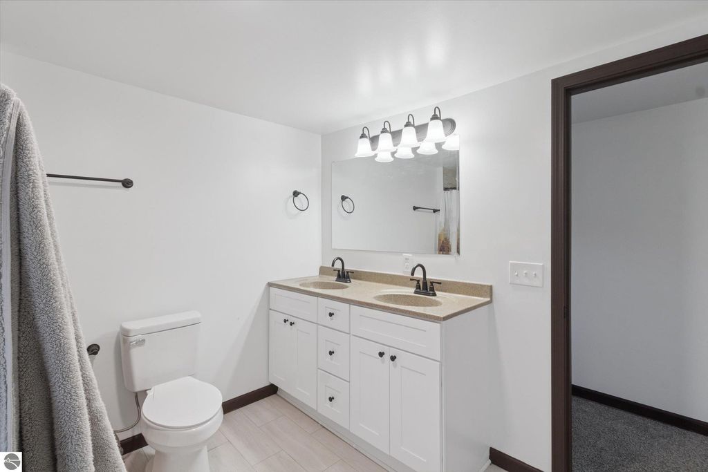Renovated bathroom featuring dual sinks, granite countertop, modern faucets, and stylish lighting, showcasing a clean and updated design in the home at 117 E Wright Avenue, Shepherd, MI.