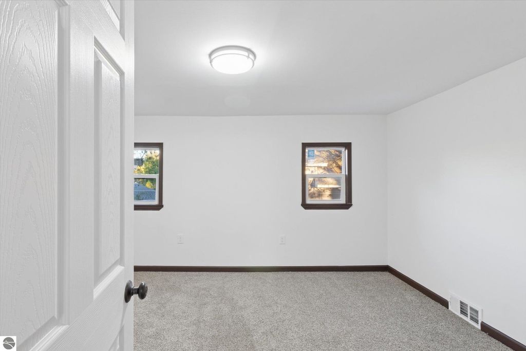Renovated interior of a bedroom in a home at 117 E Wright Avenue, featuring new carpet, white walls, and two windows with natural light.