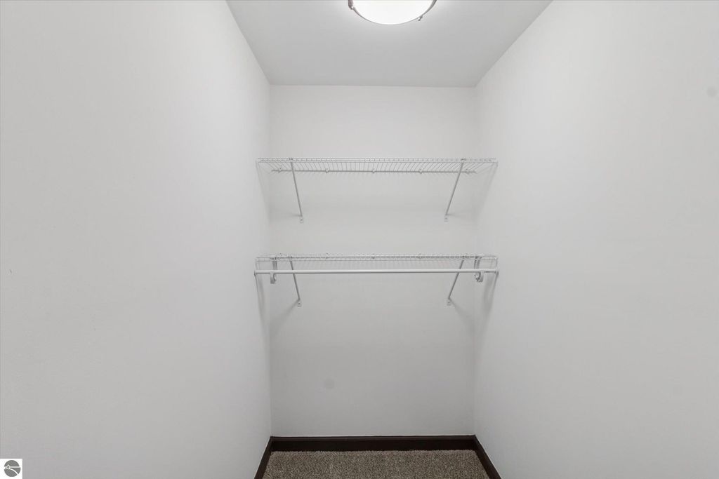 Walk-in closet with two wire shelves and neutral wall color, featuring plush carpet flooring, part of a renovated 3-bedroom home in Shepherd, MI.