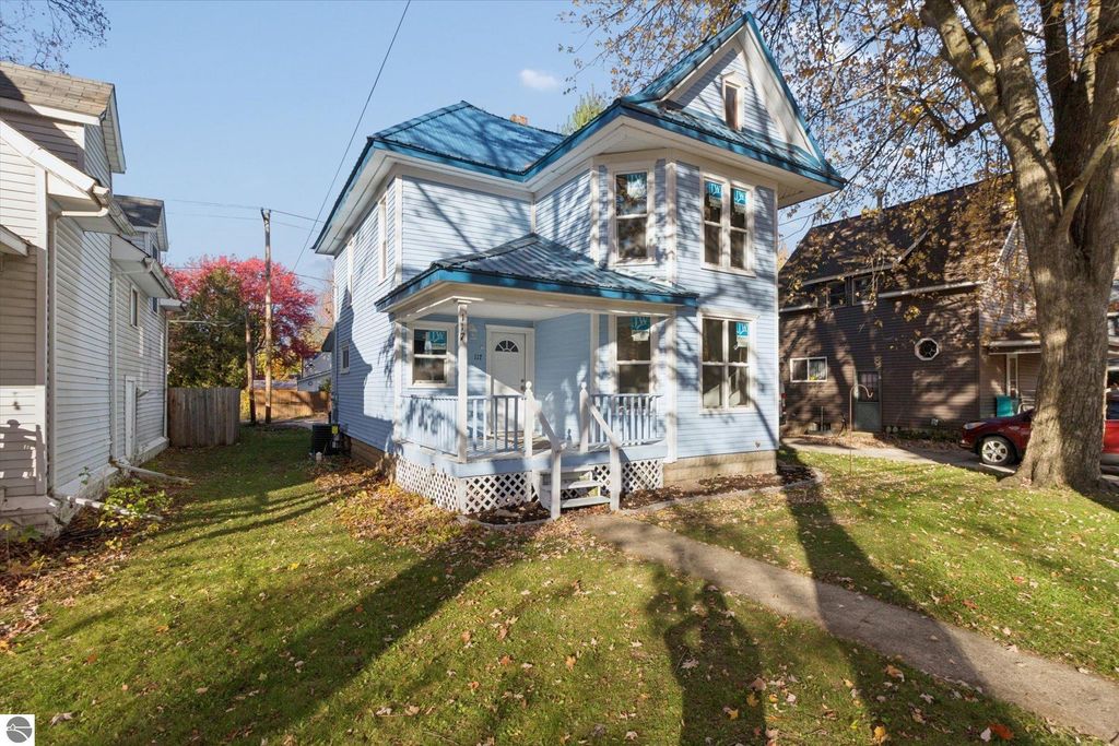 Gorgeous renovated blue house at 117 E Wright Avenue, Shepherd, MI, featuring new roof, windows, and porch, surrounded by fall foliage and neighboring homes.