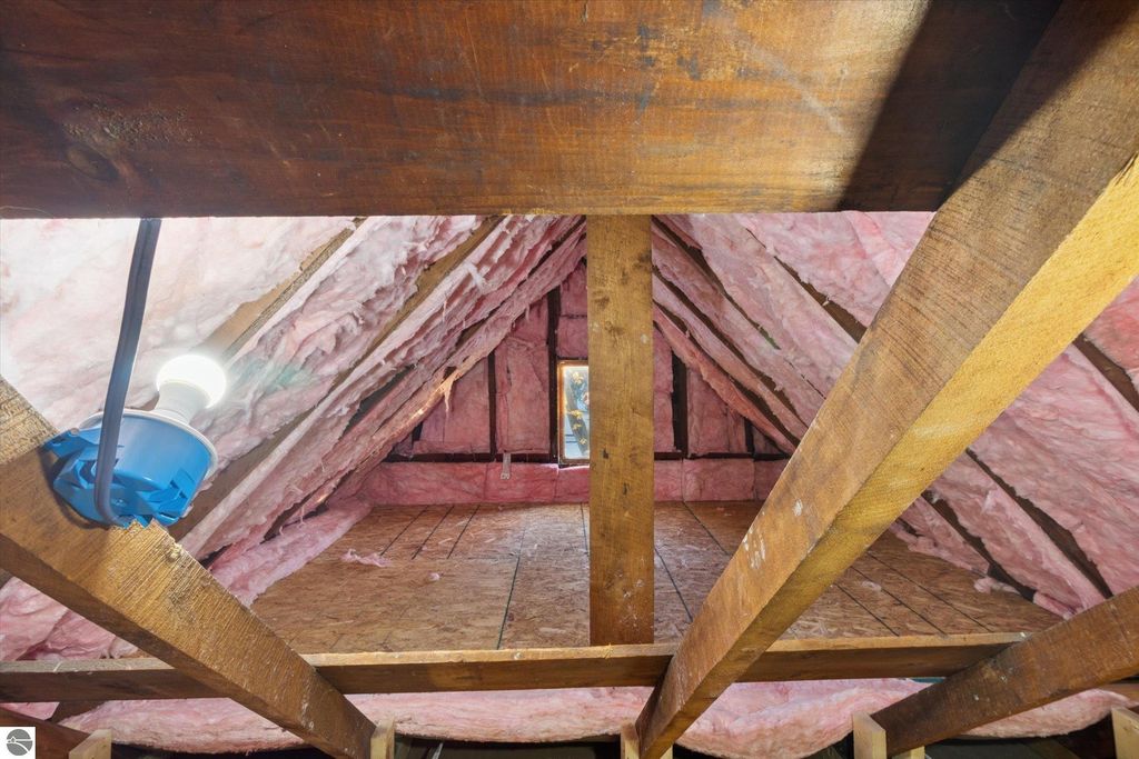Attic view showcasing insulated beams, light fixture, and pink insulation material, highlighting the recent renovations of the home at 117 E Wright Avenue, Shepherd, MI.