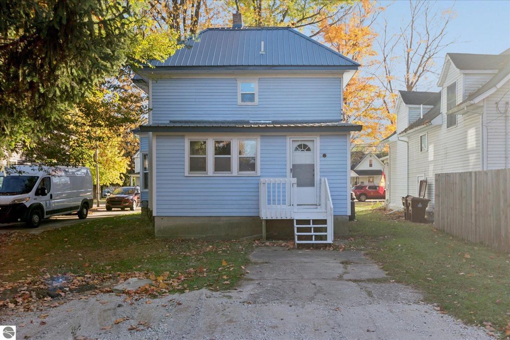 Renovated blue two-story home at 117 E Wright Avenue, Shepherd, MI, featuring new exterior, metal roof, and landscaped yard, ideal for potential buyers seeking modern living.